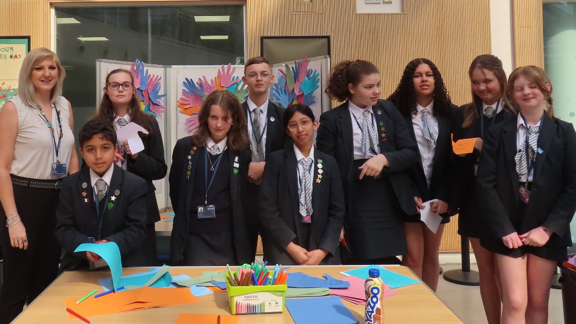 Students and a teacher at an anti-bullying event, standing near a table with colourful paper and art supplies