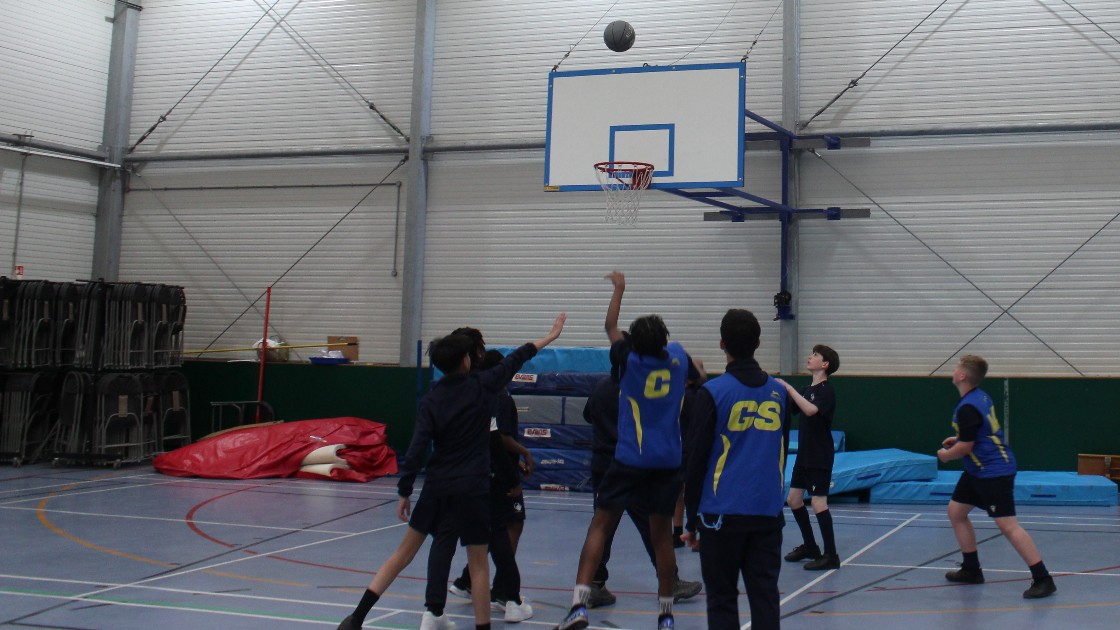 Students playing basketball in a school gym during a PE lesson