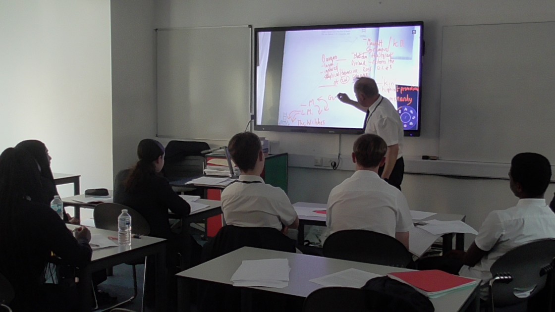 Teacher pointing at a digital whiteboard while students watch during an English lesson