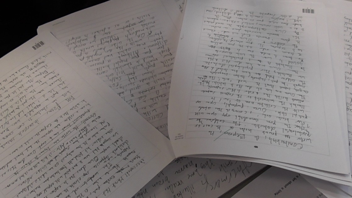 Several handwritten English assignments on lined paper, spread out on a desk