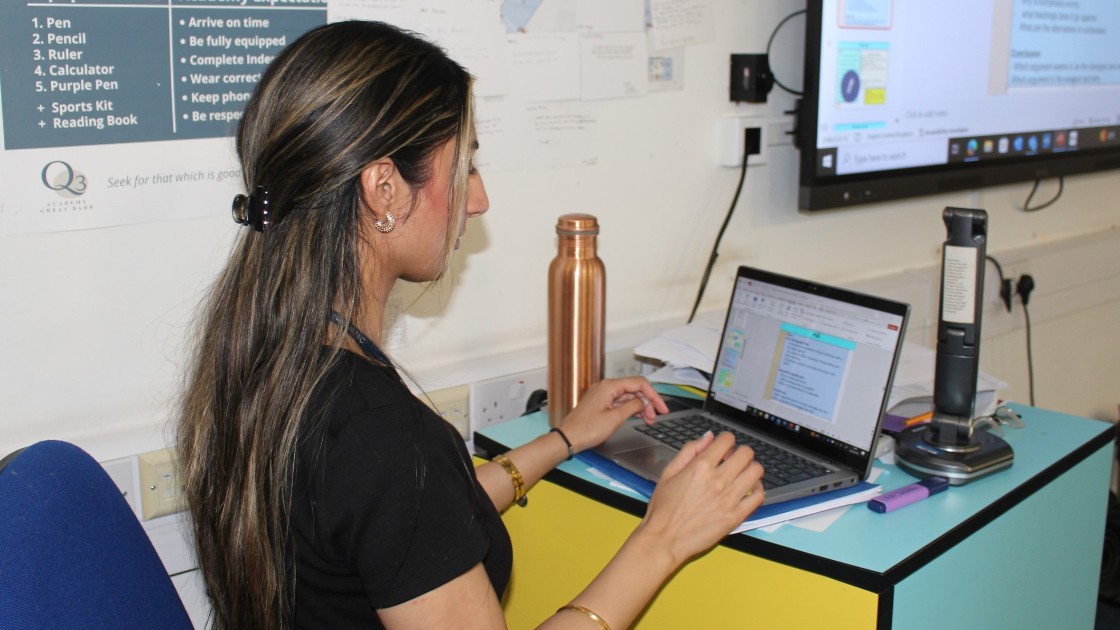 Teacher preparing a lesson on a laptop in a classroom, with a presentation on the screen