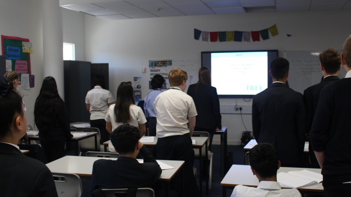 Students standing in a classroom facing a screen during an RS lesson