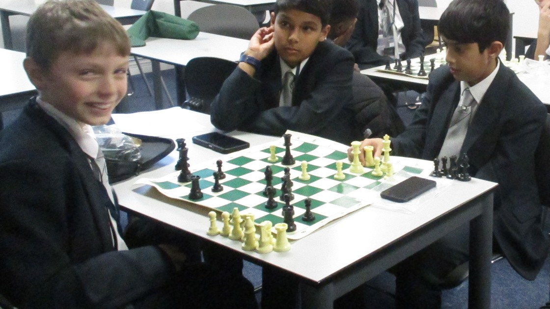 Three students in school uniform playing chess at a classroom table