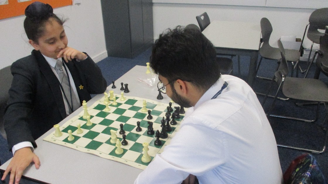 A student and a teacher playing chess at a table in a classroom