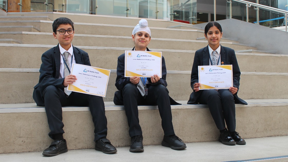 Three students showing their Junior Maths Challenge gold certificates.