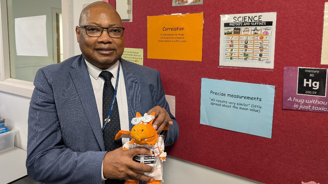 Teacher holding a science-themed toy in front of a science display board