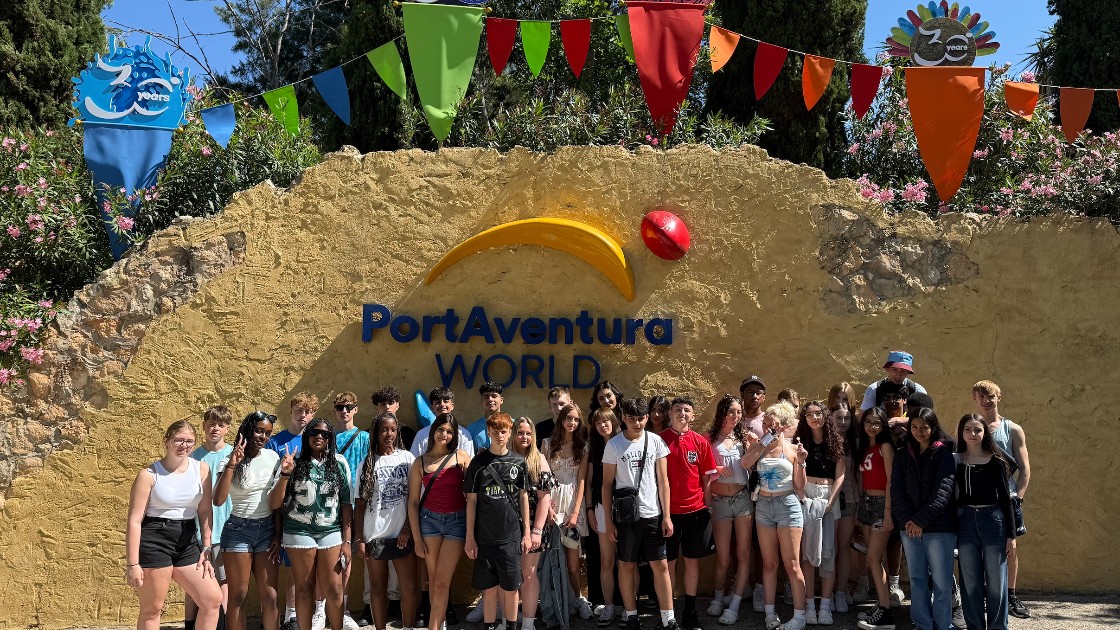 A group of students posing in front of the PortAventura World sign with colourful flags above celebrating 30 years.