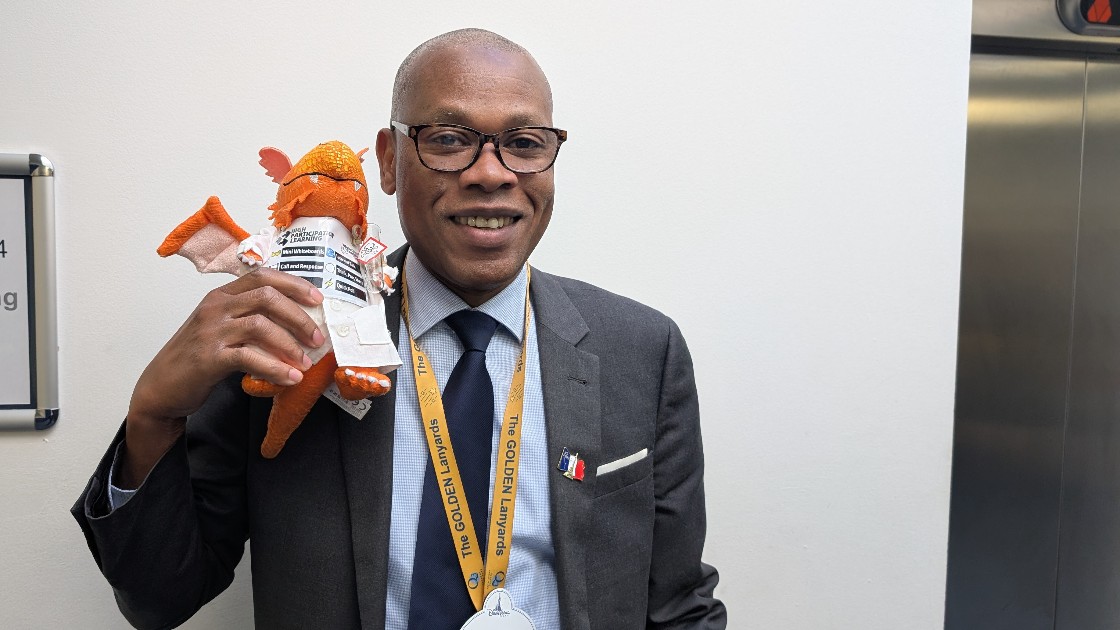 Teacher holding an orange dragon toy and smiling, standing indoors