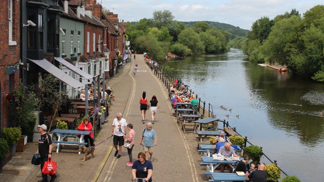 Students and teachers walking and sitting by the riverside in Bewdley, with scenic views and outdoor seating