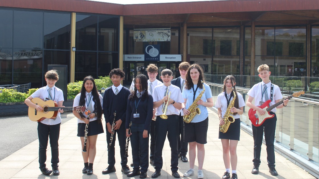 Group of students standing outside holding musical instruments including guitars, saxophones, trumpet, and clarinet