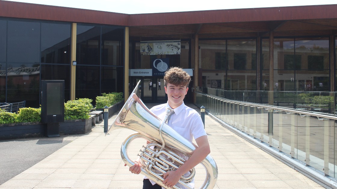 Student holding a tuba outside the academy building
