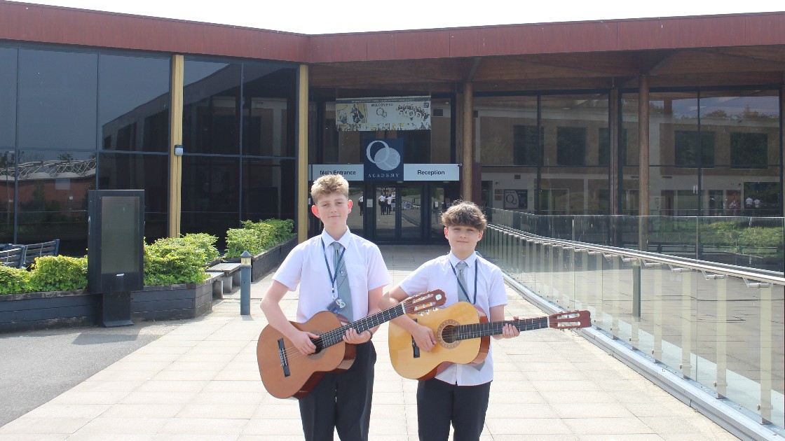 Two students holding guitars outside the Academy building