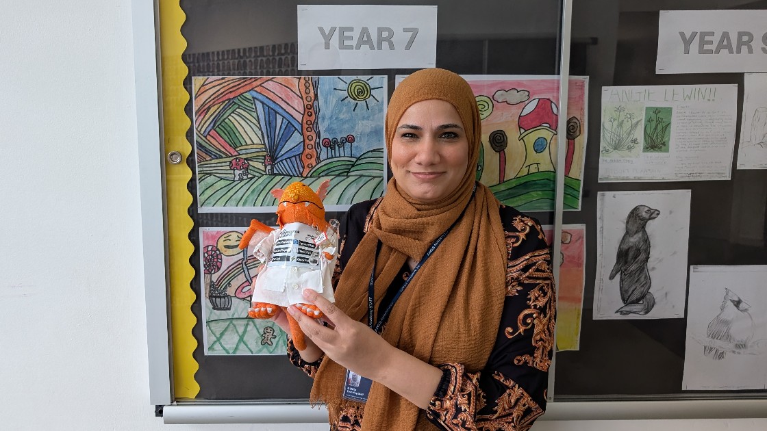 Teacher holding a creative art project in front of a Year 7 student artwork display