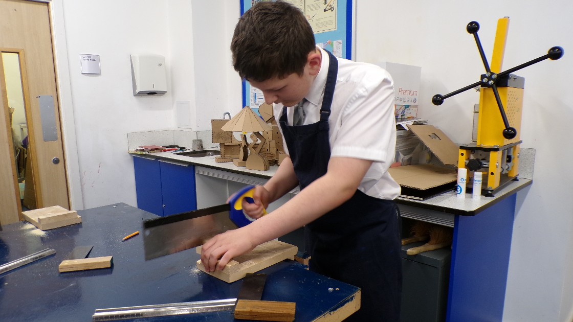 Student using a saw to cut wood in a DT classroom