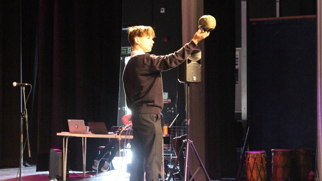 Student on stage holding a skull, performing a dramatic scene during Summer Fest Day One
