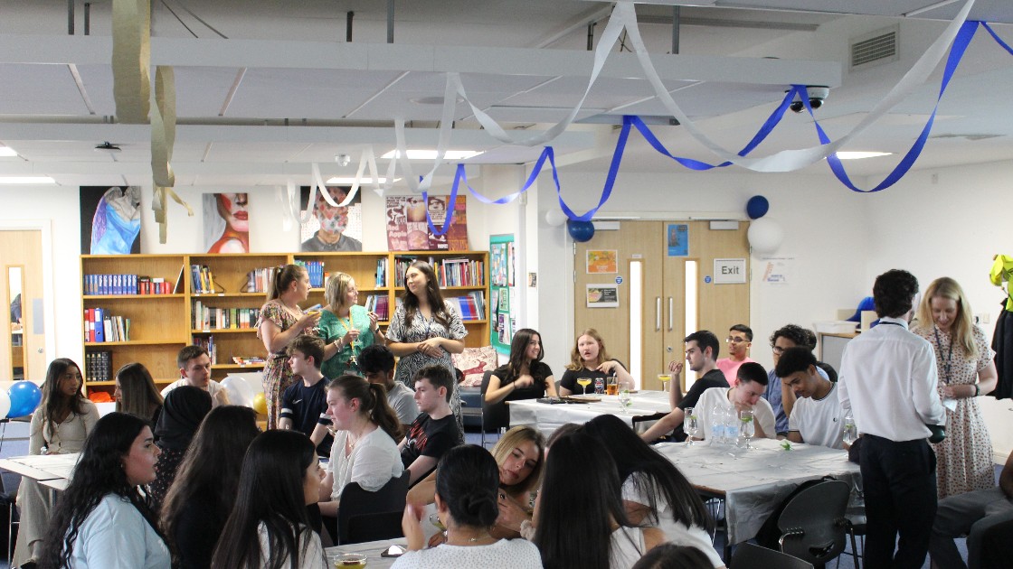 Students and teachers gathered in a decorated room for a Summer Leavers' Event, sitting and chatting around tables