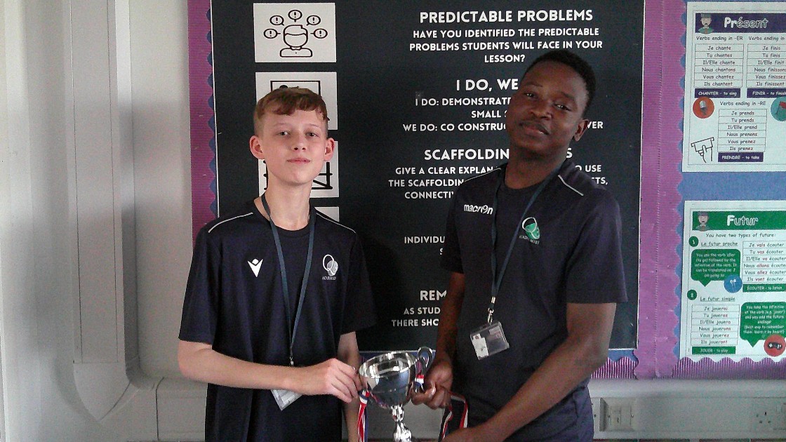 Two students holding a trophy in front of a classroom display board