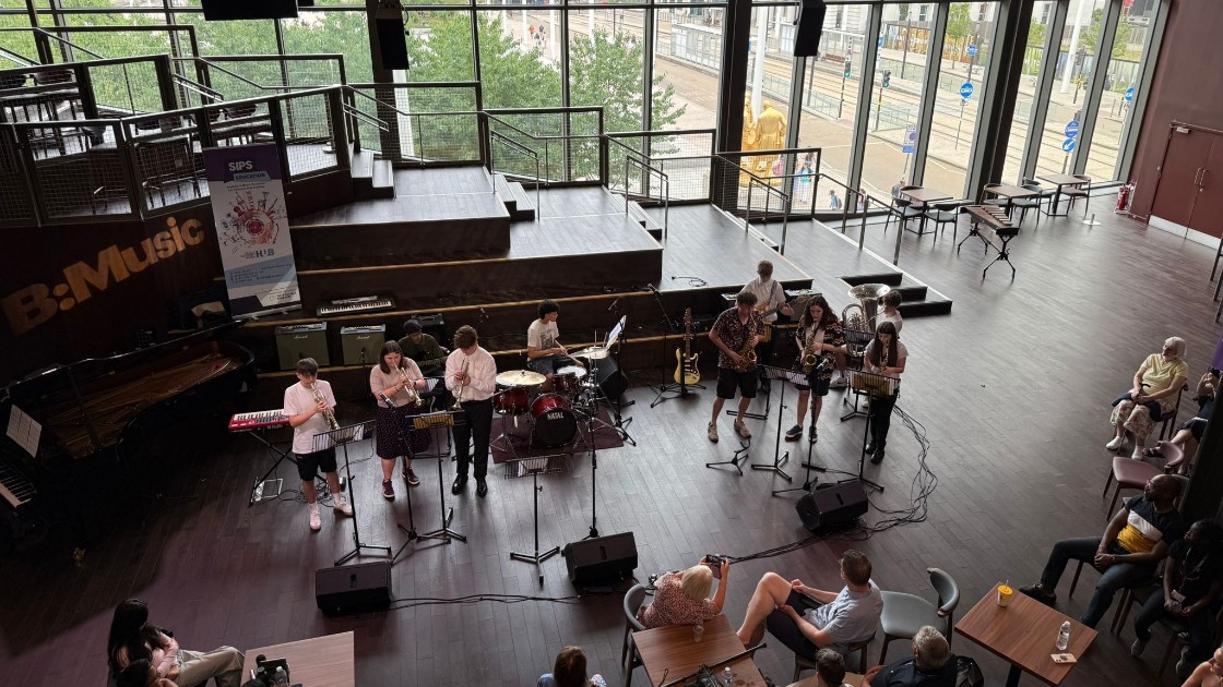 Students performing music on stage with instruments in front of an audience in a large hall