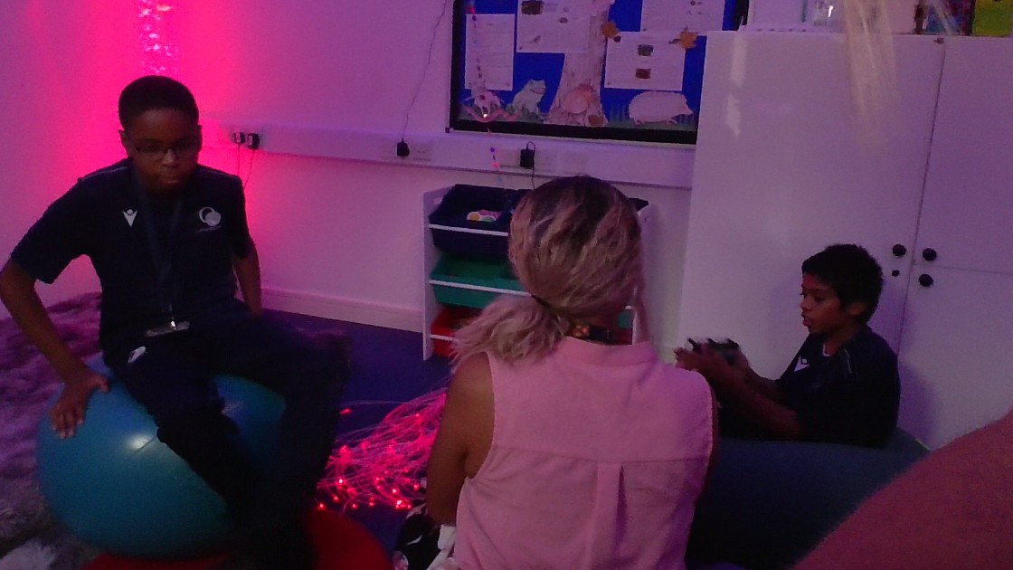 Two students and a teacher in a dimly lit sensory room with soft lighting and sensory equipment